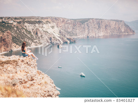 Picturesque view of the cliffs near the sea. Picture of the girl sitting on the cliff near the ocean and looking at the seascape. Picturesque view of the cliffs near the sea. Picture of the girl sitting on the cliff near the ocean and looking at the seascape. 83401827
