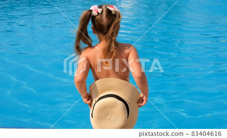 little girl stands and covers herself with a sun hat against the backdrop of the blue water of the 83404616