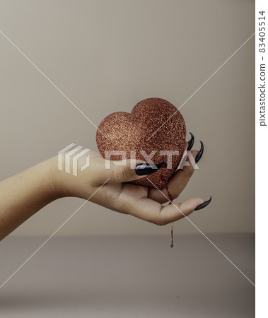 Halloween theme: hand with halloween nail polish hold torn bleeding human heart 83405514