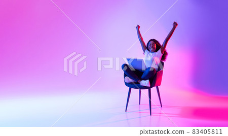 Joyful young black woman sitting in armchair with laptop, celebrating huge online win or success in neon light, banner Joyful young black woman sitting in armchair with laptop, celebrating huge online win or success in neon light, banner 83405811
