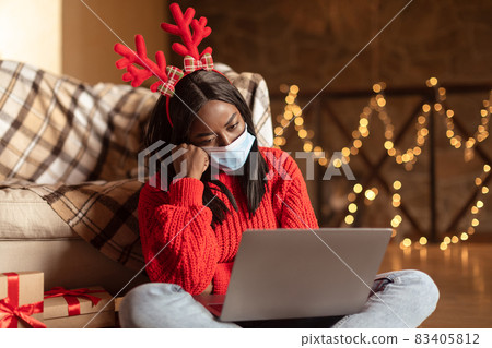 Unhappy black woman in face mask using laptop, feeling depressed celebrating Christmas alone during coronavirus Unhappy black woman in face mask using laptop, feeling depressed celebrating Christmas alone during coronavirus 83405812