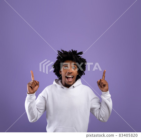 Cool black teenager pointing upwards with both hands on violet studio background, space for your ad design Cool black teenager pointing upwards with both hands on violet studio background, space for your ad design 83405820