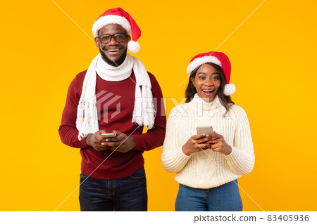African American Couple Holding Smartphones Wearing Santa Hats, Studio Shot African American Couple Holding Smartphones Wearing Santa Hats, Studio Shot 83405936