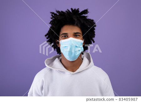 Black teenager wearing medical protective mask during coronavirus pandemic on violet studio background 83405987