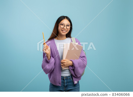 I know the answer. Excited asian female student in eyeglasses holding notepad and pointing pencil up, blue background 83406066