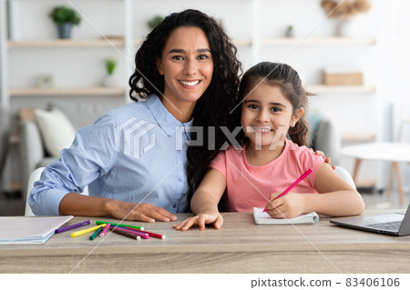Happy Mother And Little Daughter Posing At Table While Making Homework Together Happy Mother And Little Daughter Posing At Table While Making Homework Together 83406106