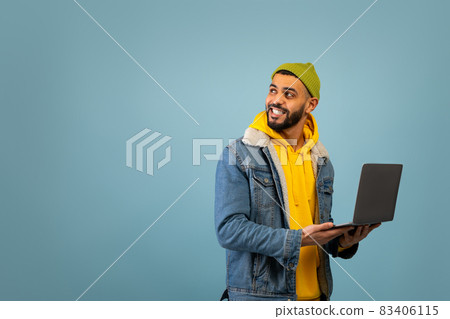 Remote job. Happy young arab guy with laptop computer looking aside at free space, standing on blue background Remote job. Happy young arab guy with laptop computer looking aside at free space, standing on blue background 83406115