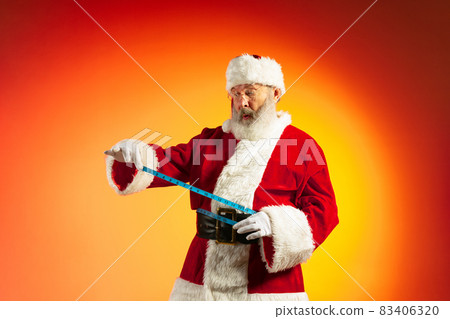 Emotional senior man, Santa Claus posing isolated on red yellow background in neon. Healthy New Year 2022 Emotional senior man, Santa Claus posing isolated on red yellow background in neon. Healthy New Year 2022 83406320