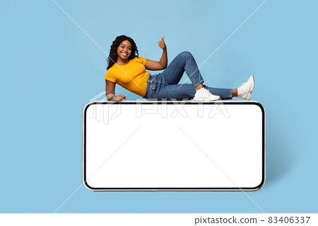 Cheerful pretty black lady chilling on smartphone with blank screen 83406337