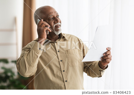 Senior African American Businessman Talking On Cellphone Holding Paper Indoors 83406423