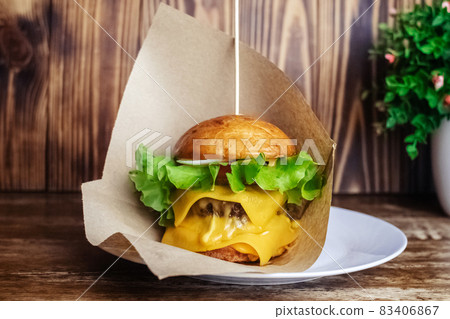 Close-up of a double burger. Adult fast food in a restaurant or cafe. Macro photo of burger ingredients with meat, cheese and herbs. Eco burgers for the whole family 83406867