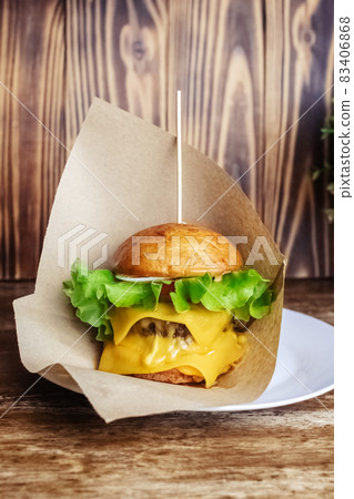 Close-up of a double burger. Adult fast food in a restaurant or cafe. Macro photo of burger ingredients with meat, cheese and herbs. Eco burgers for the whole family 83406868