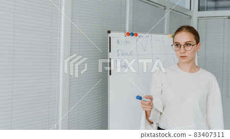 Young business woman, speaker coach drawing on white board and having online meeting in office. Focused team leader businesswoman, project manager working with white board 83407311