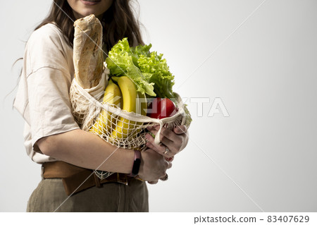 Zero waste concept with copy space. Woman holding a reusable mesh shopping bag with vegetables, products. Eco friendly mesh shopper. Zero waste, plastic free concept. Zero waste concept with copy space. Woman holding a reusable mesh shopping bag with vegetables, products. Eco friendly mesh shopper. Zero waste, plastic free concept. 83407629