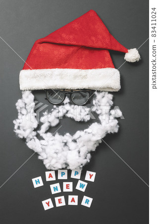 Composition with red velvet hat, glasses and fiberfill. Funny santa claus face. New Year card Composition with red velvet hat, glasses and fiberfill. Funny santa claus face. New Year card 83411024