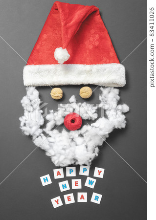 Composition with Santa's hat, walnuts, a ball of thread and fiberfill. Funny santa claus face. New Year card Composition with Santa's hat, walnuts, a ball of thread and fiberfill. Funny santa claus face. New Year card 83411026