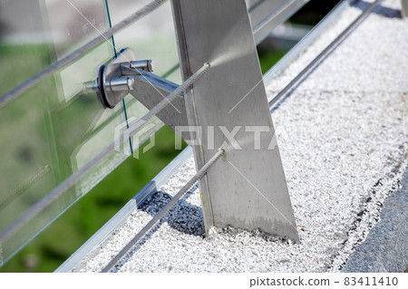metal turnbuckles fastening of cables with steel rod on pedestrian bridge with stone pebble path and glass barrier for safety close-up details of construction on sunny day, nobody. 83411410