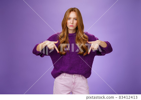 Woman dissatisfied with bad quality of service. Portrait of upset disappointed redhead female frowning and sulking as pointing down demanding explanations of bad product over violet wall 83412413