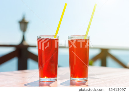 Two glasses with berry juice and strawberries on the table of a street cafe against the background of the sea Two glasses with berry juice and strawberries on the table of a street cafe against the background of the sea 83413097