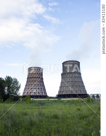 Thermal power station, cogeneration plant, two cooling towers from which smoke comes. Green grass, blue sky. Place for text. Vertical photo 83413180