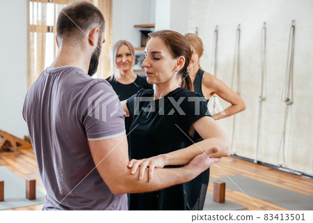 Yoga Trainer helping woman to stand on sadhu yoga board during yoga class, barefoot on a bed of nails 83413501