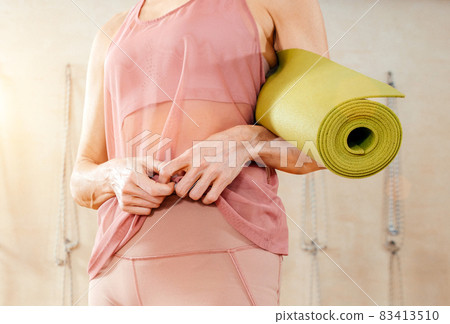 Woman wearing activewear standing in gym holding yoga mat ready to start fitness or yoga training. Concept of sports lifestyle. Yoga concept 83413510
