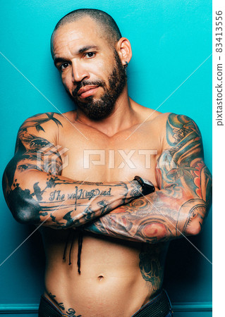 A middle-aged Cuban man with a muscular torso stands near the wall and looks directly into the 83413556