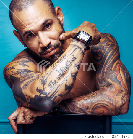 A swarthy brutal man. Naked muscular body with tattoos. Studio portrait of a Cuban or Latino. Looks 83413582