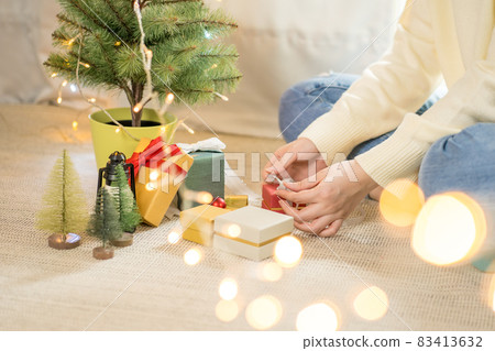 woman hand tieding ribbon new year gift box and decorate christmas tree woman hand tieding ribbon new year gift box and decorate christmas tree 83413632