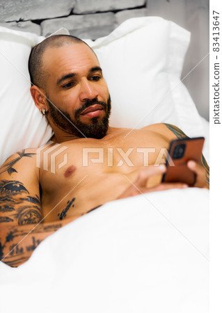A bearded man lies in the post and corresponds on the phone. A sexy Cuban with a naked torso looks 83413647