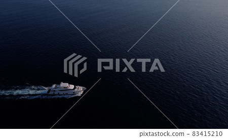 White luxury yacht sails on the ocean. Shooting from a drone as a small light sea vessel, leaving a trail of foam and waves along the sea dark water surface White luxury yacht sails on the ocean. Shooting from a drone as a small light sea vessel, leaving a trail of foam and waves along the sea dark water surface 83415210