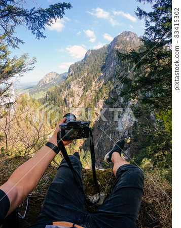 A photographer observes with his camera in hand from the top of a mountain. 83415302