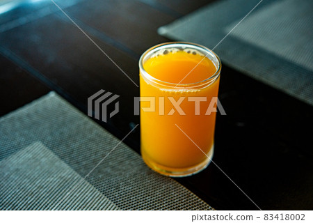 Orange juice in a glass Full glass of orange juice close-up. Fresh orange juice on wooden table in out of focus unidentified restaurant in the morning in summer Orange juice in a glass Full glass of orange juice close-up. Fresh orange juice on wooden table in out of focus unidentified restaurant in the morning in summer 83418002