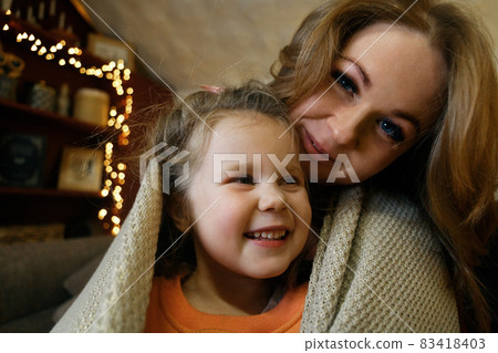 Close-up portrait of blond funny little girl with her mother in festive interior with garlands Close-up portrait of blond funny little girl with her mother in festive interior with garlands 83418403