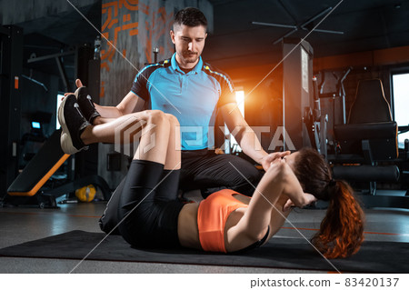 young woman exercising abs crunches with personal trainer in gym 83420137