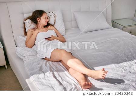 Happy woman lies in bed and holds smartphone. Happy woman lies in bed and holds smartphone. 83420348