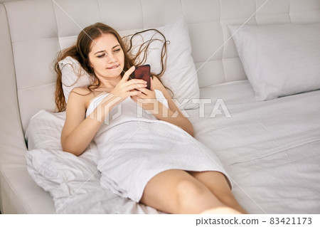 Elegant naked woman lies in bed with mobile phone. Elegant naked woman lies in bed with mobile phone. 83421173