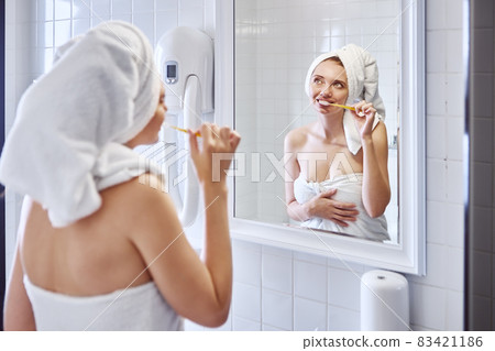 Woman brushes teeth in bathroom near mirror. 83421186