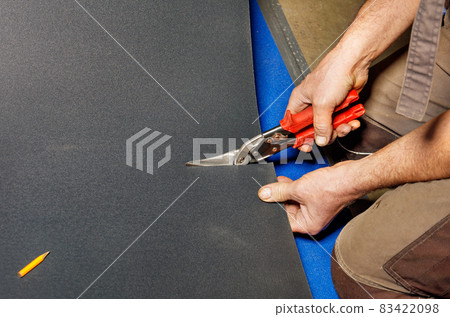A worker cuts a sheet of roofing iron with metal scissors. 83422098