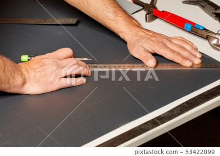 A worker marks out a sheet of roofing iron with a pencil and a ruler. 83422099