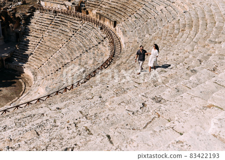 A couple runs down the stairs of the Pamukkale Amphitheater in Turkey. A man and a woman are traveling in Turkey. The couple travels the world. Tourists in Turkey. Amphitheater in Pamukkale Denizli 83422193