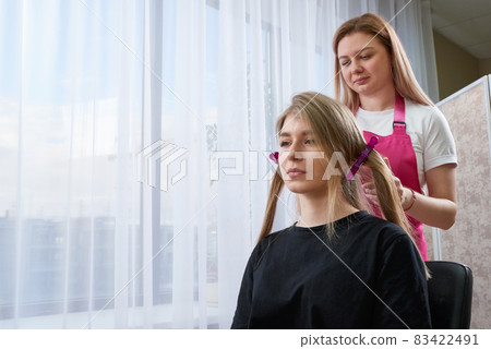 Hairdresser makes hairstyle girl with long hair in a beauty salon. Create curls with curling irons 83422491