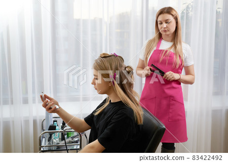 Hairdresser makes hairstyle girl with long hair in a beauty salon. Create curls with curling irons Hairdresser makes hairstyle girl with long hair in a beauty salon. Create curls with curling irons 83422492
