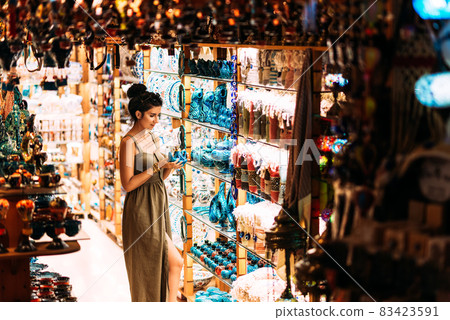 Beautiful girl in a souvenir shop in Turkey. Girl chooses a souvenir. Oriental shop. Turkish Souvenirs. Oriental bazaar. Turkish Bazaar. Gift shop in Goreme, Turkey. Moroccan Bazaar. Copy space. 83423591