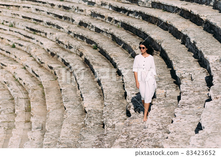 Girl walking on the steps of an ancient amphitheater, located in Hierapolis, Pamukkale, Denizli province, Turkey. Beautiful girl on the steps. Girl in white dress on stone stairs 83423652