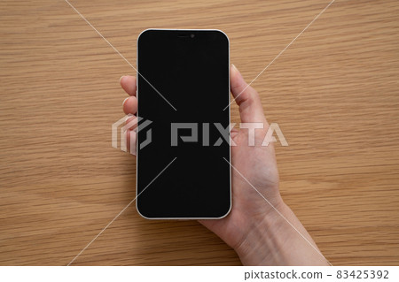 A woman holding a smartphone on a wooden desk [Parts cut] 83425392