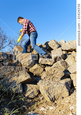 a man works with a pile of stones and broken pieces of concrete, carries construction debris a man works with a pile of stones and broken pieces of concrete, carries construction debris 83426556
