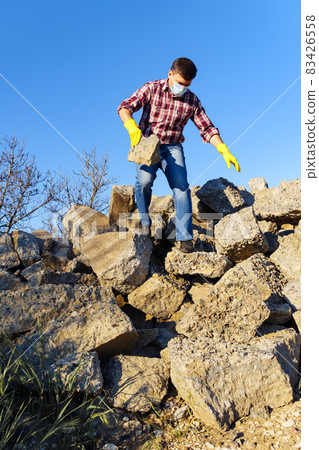 a man works with a pile of stones and broken pieces of concrete, carries construction debris a man works with a pile of stones and broken pieces of concrete, carries construction debris 83426558