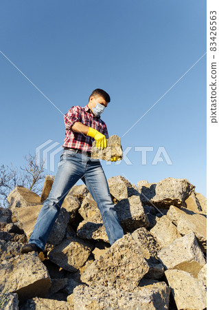 a man works with a pile of stones and broken pieces of concrete, carries construction debris 83426563