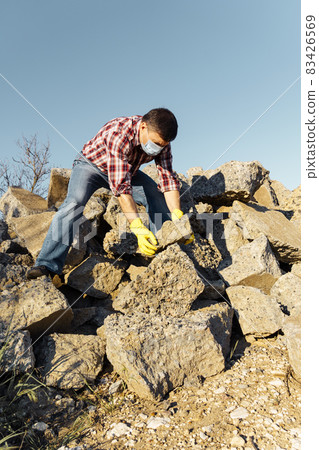 a man works with a pile of stones and broken pieces of concrete, carries construction debris a man works with a pile of stones and broken pieces of concrete, carries construction debris 83426569